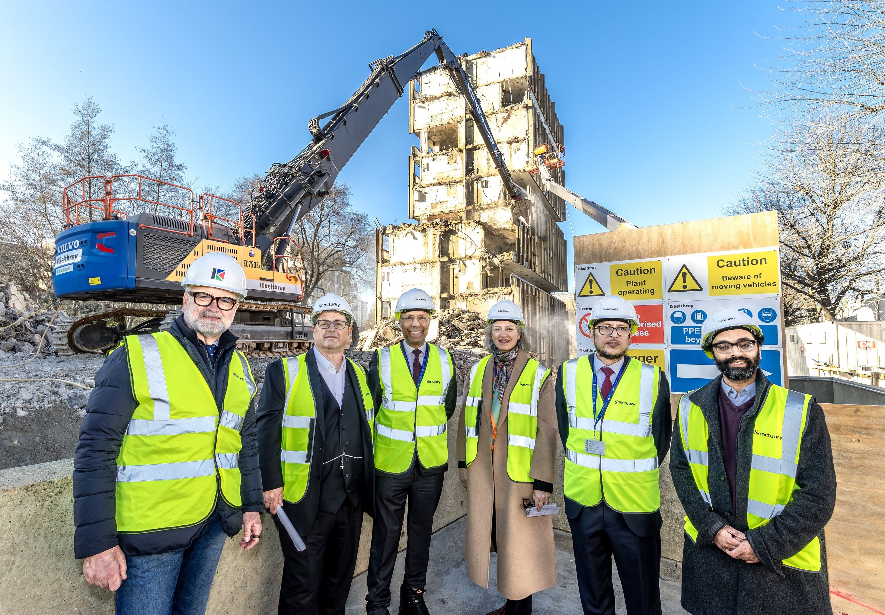 Six people wearing hard hats and high vis in front of a building demolition site