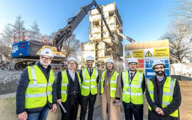 Six people wearing hard hats and high vis in front of a building demolition site