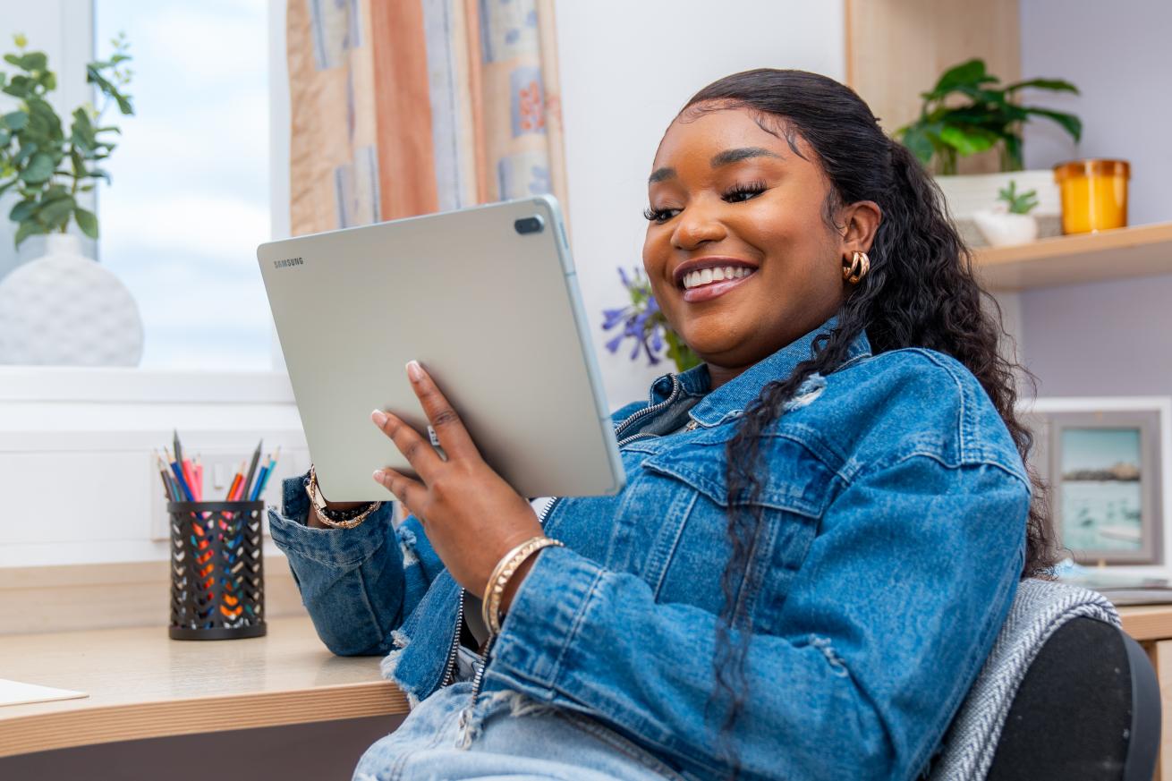 A young woman sits at her desk looking at a tablet