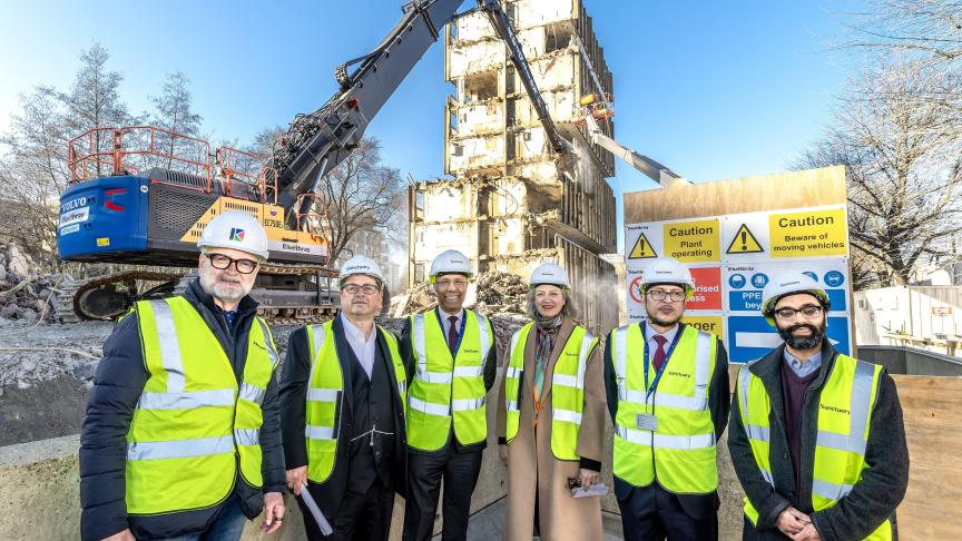 Six people wearing hard hats and high vis in front of a building demolition site