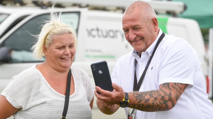 Two people chatting near a white van—one shows something on their phone. The van says “A better life, no conditions.” Two people chatting near a white van—one shows something on their phone. The van says “A better life, no conditions.”