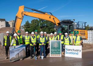 A group of 14 people wearing high vis and hard hats stood in front of a housing development site on a sunny day