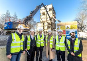 Six people wearing hard hats and high vis in front of a building demolition site